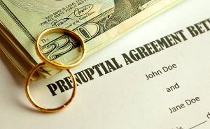 money and wedding rings on top of a document that reads prenuptial agreement